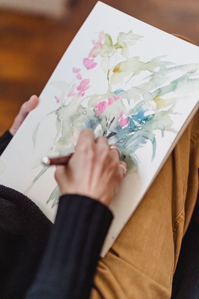 A person painting delicate floral watercolor art in a sketchbook, showcasing creativity and imagination.